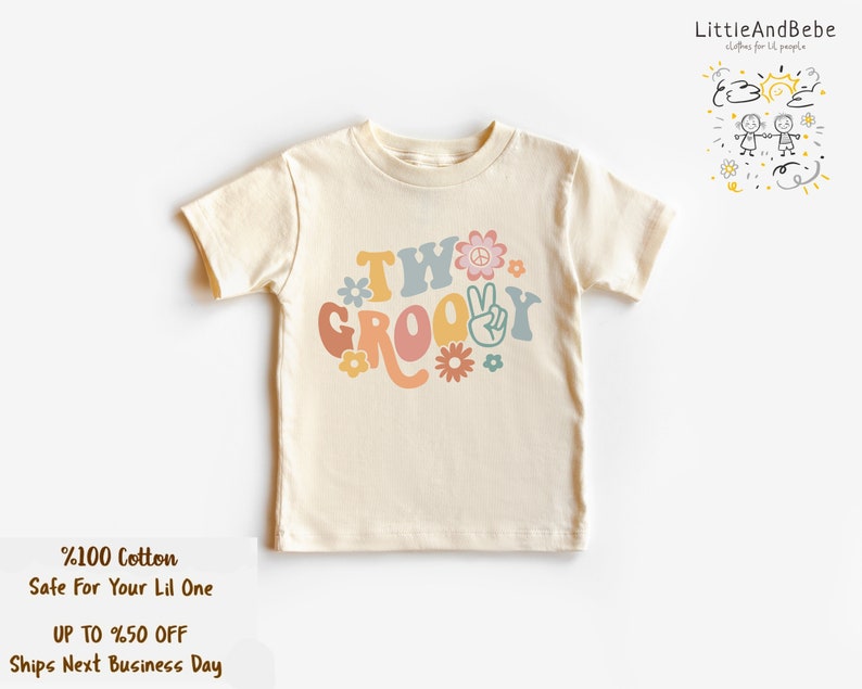 May include: A cream colored short-sleeved t-shirt with the text "Two Groovy" in colorful retro font with peace signs and flowers.