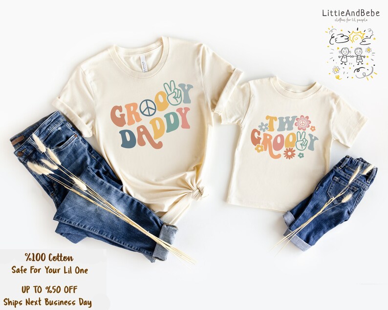 May include: Two matching t-shirts with a retro groovy design. The larger shirt says "Groovy Daddy" in rainbow colors with a peace sign. The smaller shirt says "Two Groovy" in rainbow colors with a peace sign and flowers.