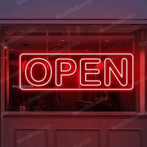 Könnte beinhalten: Ein rotes Neon-Schild mit dem Wort "OFFEN" in einem rechteckigen Rahmen, das in einem Schaufenster ausgestellt ist.