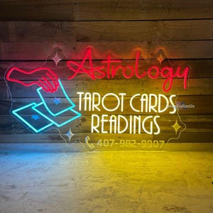 May include: Neon sign with the words "Astrology Tarot Cards Readings" and a phone number, 407-982-9907. The sign is lit in pink, yellow, and blue.