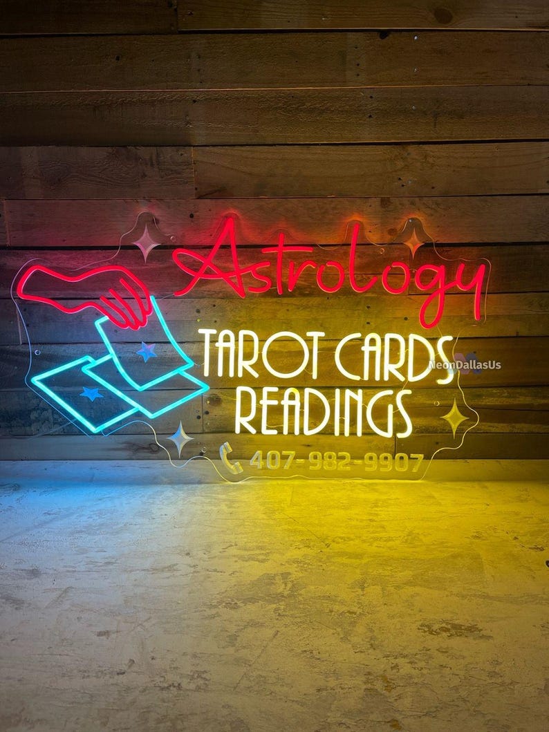 May include: Neon sign with the words "Astrology Tarot Cards Readings" and a phone number, 407-982-9907. The sign is lit in pink, yellow, and blue.