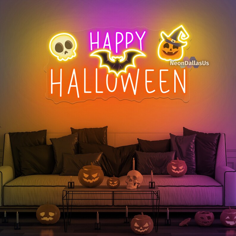 Op de afbeelding: Een neonbord met de woorden "HAPPY HALLOWEEN" in het wit, met schedel-, vleermuis- en pompoen-iconen. Het bord hangt aan een oranje muur boven een bank met zwarte kussens en Halloween-decoraties.