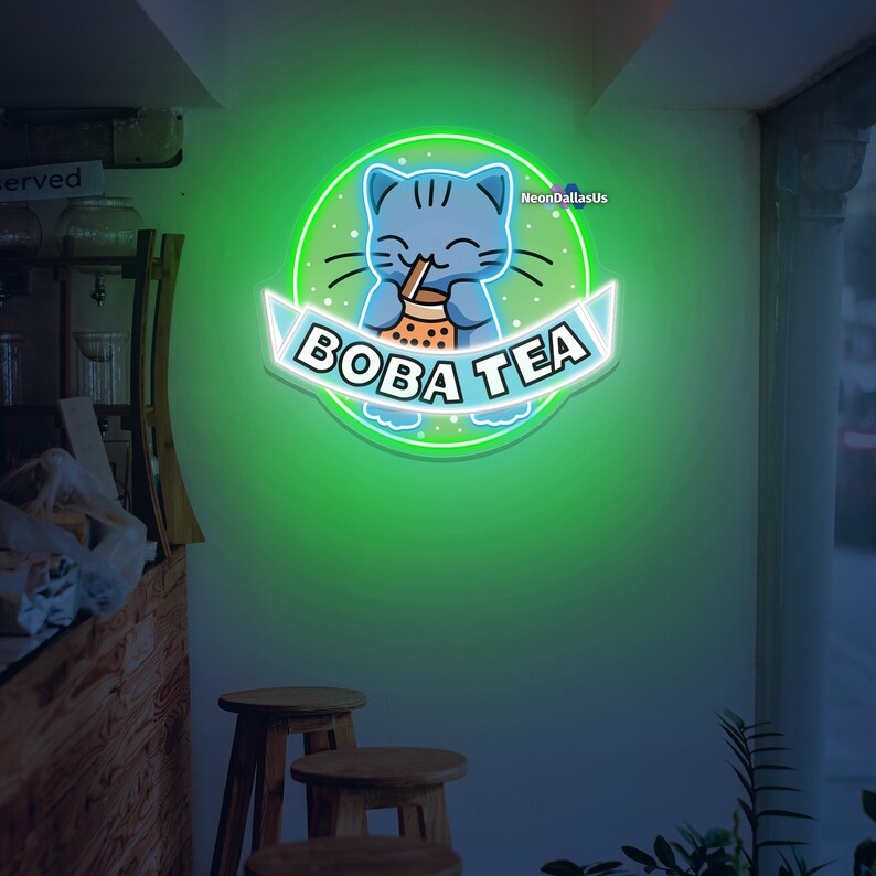 May include: Neon sign with a green background and a blue cat holding a boba tea cup. The sign says "BOBA TEA" in a white banner.
