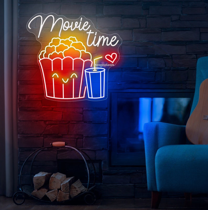 Op de afbeelding: Neon-bord met de woorden "Movie time" in witte letters. Het bord toont ook een cartoon-afbeelding van een emmer popcorn met een glimlachend gezicht en een blauwe drank met een rietje. Het bord licht op in rood, geel en blauw.