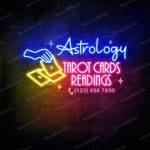 May include: Neon sign with a blue hand holding two yellow tarot cards. The sign reads "Astrology Tarot Cards Readings (123) 456 7890".