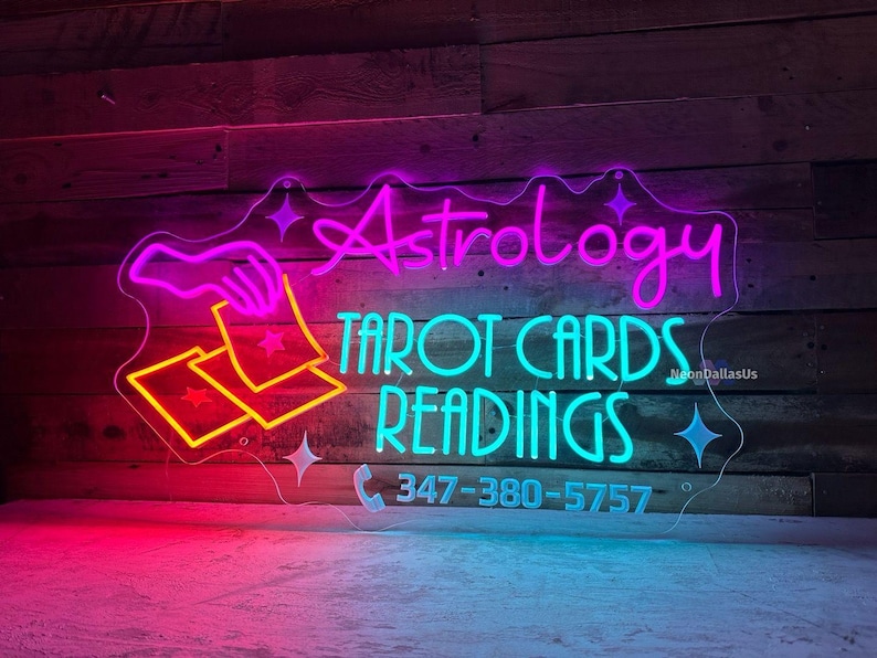 May include: Neon sign with a pink "Astrology" and turquoise "Tarot Cards Readings" text. A hand holding two cards with stars is depicted. The phone number 347-380-5757 is also included.