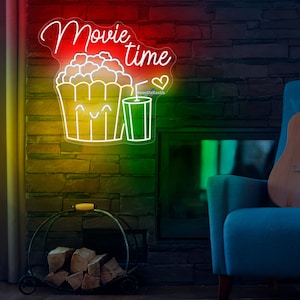 Op de afbeelding: Neon-bord met de woorden "Movie time" in wit, cursief schrift. Het bord bevat ook een cartoonafbeelding van een emmer popcorn met een vrolijk gezicht en een glas frisdrank. Het bord is verlicht in rood, geel en groen.