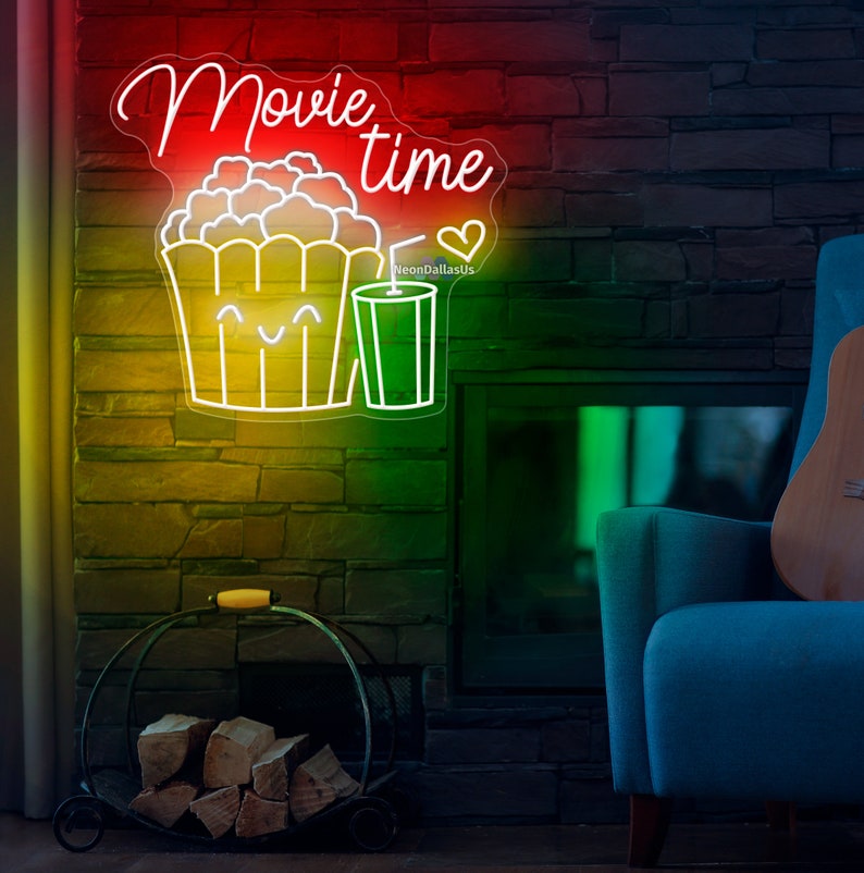 Op de afbeelding: Neon-bord met de woorden "Movie time" in wit, cursief schrift. Het bord bevat ook een cartoonafbeelding van een emmer popcorn met een vrolijk gezicht en een glas frisdrank. Het bord is verlicht in rood, geel en groen.