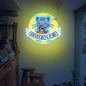 May include: A neon sign with a yellow background and a blue cat drinking boba tea. The sign says "Boba Tea" in a white banner.