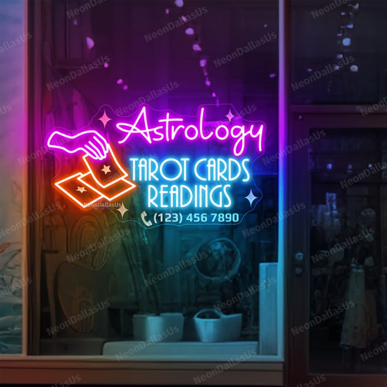 May include: Neon sign with a pink, blue, and orange color scheme advertising tarot card readings and astrology. The sign features a hand holding two tarot cards and the text "Astrology Tarot Cards Readings (123) 456 7890".