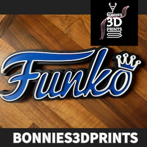 Può includere: Un logo Funko Pop stampato in 3D con un design blu e bianco. Il logo è su una superficie di legno. Il logo è realizzato da Bonnie's 3D Prints.