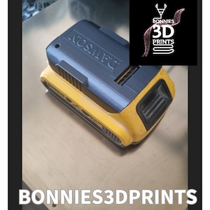 May include: A black and yellow DeWalt battery with the text "DeWalt" printed on the top. The battery is sitting on a wooden surface. The image also includes a logo for "Bonnies 3D Prints" in the top right corner.