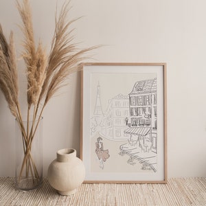 May include: A framed art print featuring a line drawing of a Parisian street scene with the Eiffel Tower in the background. The artwork depicts a person riding a bicycle, with buildings and a cafe. The frame is made of light-colored wood.