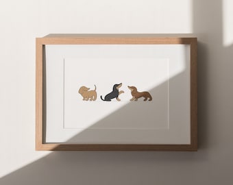 May include: A framed print featuring three cartoon dachshunds in various poses. The dogs are depicted in shades of brown and black against a white background. The frame is made of light-colored wood, adding a natural touch to the artwork. The print is displayed on a white wall.