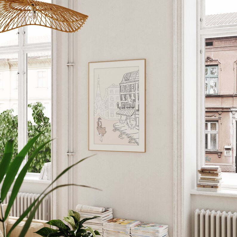 May include: A framed art print featuring a black and white line drawing of a European street scene with a woman in a dress. The artwork includes the Eiffel Tower and buildings with awnings. The frame is gold-toned.