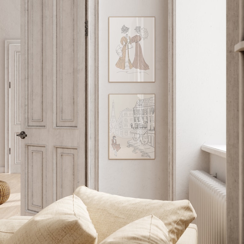 May include: Two framed art prints featuring line drawings. The top print depicts two women in vintage dresses with parasols. The bottom print shows a Parisian street scene with the Eiffel Tower. Both prints have a neutral color palette.