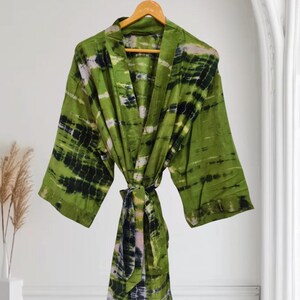 May include: A green kimono robe featuring a tie-dye pattern with black and white horizontal stripes. The garment has wide sleeves, an open front, and a matching fabric tie belt at the waist, all displayed on a wooden hanger for a clear view.