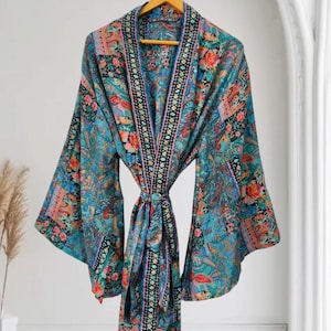 Puede incluir: Una bata tipo kimono de manga larga con una base de color verde azulado vibrante y un estampado floral y de cachemira multicolor. La prenda incluye un borde geométrico en blanco y negro que contrasta a lo largo de la abertura frontal.