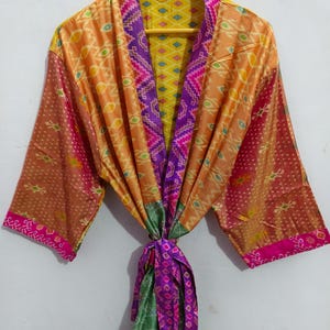 Può includere: Una vestaglia di seta colorata con un motivo geometrico in tonalità di arancione, rosa, verde e viola. La vestaglia ha una cintura a nodo e maniche lunghe.