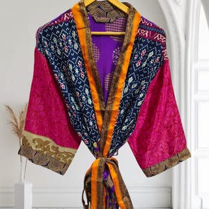 May include: A colourful silk robe with a patchwork design. The robe has a purple lining, a gold and orange sash, and a pink, blue and gold patterned fabric.