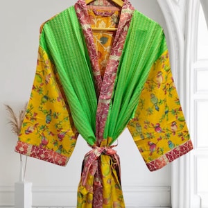 May include: A vibrant, patterned robe with a yellow, green, and burgundy color scheme. The robe features a bird and floral design on the sleeves and a textured green panel on the front. The robe is tied at the waist with a matching sash.