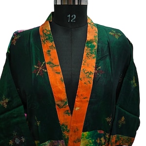May include: A green and orange silk robe with a tie belt. The robe has a patchwork design with floral patterns and embroidery. The robe is on a mannequin.