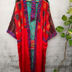 Op de afbeelding: Een lange rode kimono met een kleurrijk patchwork-ontwerp. De kimono heeft een V-hals en lange mouwen. De stof is een mix van zijde en katoen.