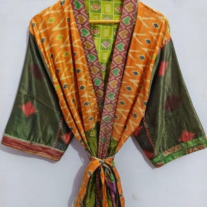 May include: A long, green, orange, and red patterned silk robe with a tie belt. The robe is made of recycled saris and has a unique, vintage style.