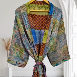 Pode incluir: Uma bata de seda colorida com um design de patchwork que apresenta padrões florais, formas geométricas e um padrão xadrez. A bata tem um cinto para amarrar e mangas compridas.