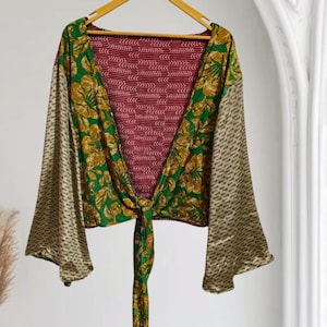 May include: A long-sleeved wrap top featuring a deep V-neckline and a front tie closure. The garment displays a mix of patterns, including a green and gold floral print on the front panels, beige patterned sleeves, and a dark red chevron back.