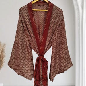 May include: A long-sleeved robe featuring a brown and tan repeating pattern across the body and wide sleeves. The garment includes a solid dark red shawl collar and a matching tie belt, both decorated with a thin, light-coloured line art design.