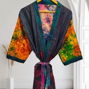 Pode incluir: Uma bata de seda colorida com cinto de laço. A bata é feita de tecido patchwork com diferentes padrões de tie-dye em tons de azul, verde, laranja, amarelo e rosa.