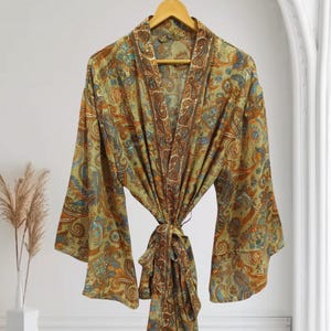 Könnte beinhalten: Ein Paisley-Muster-Robe in den Farbtönen Olivgrün, Braun und Orange hängt an einem Holzbügel. Die Robe hat weite Ärmel und einen Bindverschluss in der Taille. Der Stoff hat ein detailliertes, verziertes Design.