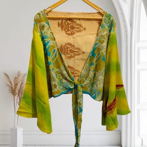May include: A green and blue patterned silk top with a tie front and long bell sleeves. The top is on a hanger against a white background.