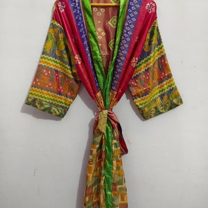 May include: A colorful silk robe with a green trim and a tie belt. The robe is made of patchwork fabric with different patterns and colors.