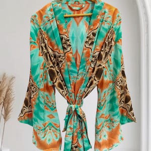 May include: A vibrant, patterned robe in shades of teal, orange, and brown, hanging on a wooden hanger. The robe features a tie closure at the waist and wide sleeves. The design has a geometric and abstract pattern.