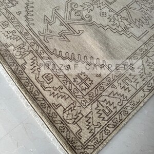 Peut inclure: Tapis beige et marron &agrave; motifs g&eacute;om&eacute;triques. Le tapis pr&eacute;sente une bordure d&eacute;taill&eacute;e et des franges sur le bord. Le texte "NAZIF CARPETS" est visible sur le tapis.