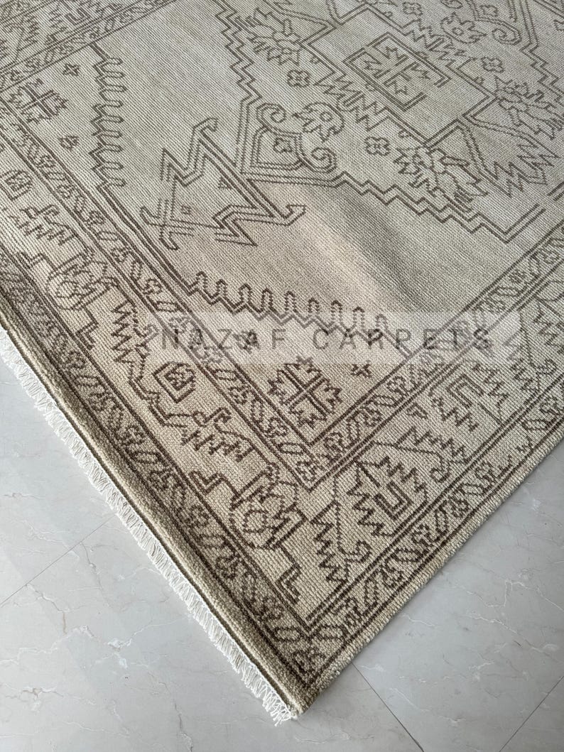 Peut inclure: Tapis beige et marron &agrave; motifs g&eacute;om&eacute;triques. Le tapis pr&eacute;sente une bordure d&eacute;taill&eacute;e et des franges sur le bord. Le texte "NAZIF CARPETS" est visible sur le tapis.