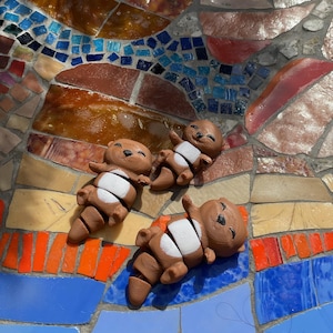 May include: Three brown and white ceramic otter figurines with segmented bodies, lying on a colourful mosaic tile surface.