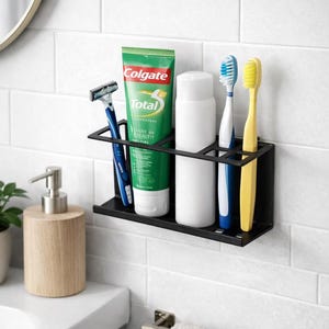 May include: A black metal bathroom organizer holding a tube of Colgate Total toothpaste, a razor, a white bottle, and two toothbrushes. The toothbrushes are blue and yellow. The organizer is mounted on a white tiled wall.