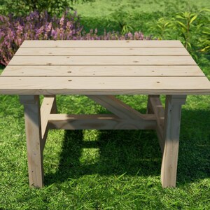 May include: A light wood square table with a simple design, featuring a flat top and four legs. The table is sitting on a green grassy lawn.