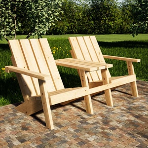 Puede incluir: Dos sillas de madera con una mesa pequeña entre ellas, colocadas en un patio de adoquines. Las sillas son de madera natural y tienen un diseño sencillo. Las sillas están enfrentadas y la mesa está en el medio. Las sillas están en un área de césped con árboles en el fondo.