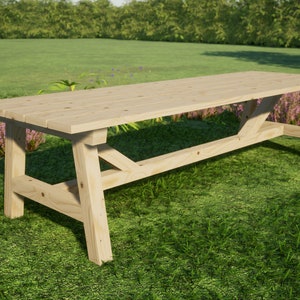May include: A long, wooden table with a natural finish sits on a grassy lawn. The table has a simple, rectangular design with a wide, flat top and sturdy legs.