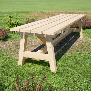 May include: A long wooden table with a natural finish and a simple design. The table is made of planks of wood and has a rectangular shape. The table is sitting on a grassy lawn.