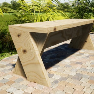 May include: A wooden bench with a simple, modern design. The bench is made of light-colored wood and has a slightly angled top. It is sitting on a brick patio.