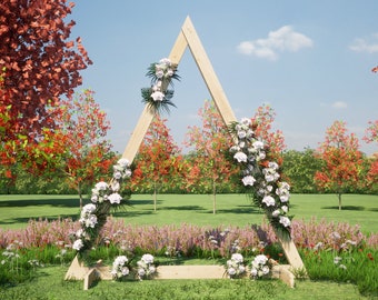 May include: A wooden triangular archway decorated with white flowers and greenery, standing in a grassy field with trees in the background.