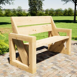 May include: A light-coloured wooden bench with a back and armrests. The bench is constructed from planks of wood and has a simple, modern design. It is placed on a brick patio, with a grassy area and trees in the background.