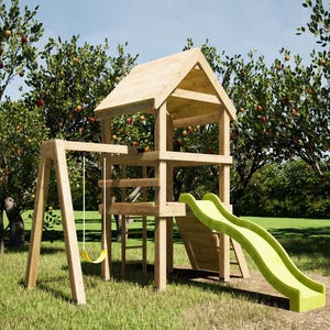 Op de afbeelding: Een houten speelset met een schommel, glijbaan en een kleine huisstructuur. De glijbaan is lichtgroen. De speelset staat in een grasveld met bomen op de achtergrond met rode vruchten.
