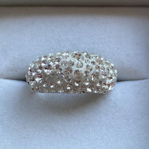 May include: A silver ring with a white band covered in small, clear rhinestones.