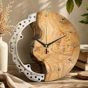 Puede incluir: Un reloj de pared circular con una esfera de madera natural con vetas visibles y un borde exterior metálico, curvo y perforado, fijado con tornillos plateados. El reloj tiene tres manecillas negras delgadas centradas en la madera.